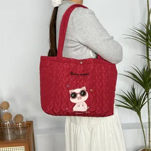 Gedetailleerd overzicht van rode gewatteerde tas met schattig varkensborduurwerk.