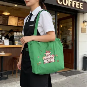 Vista detallada del bolso tote de lona verde con cerdito bordado llevado en el café.