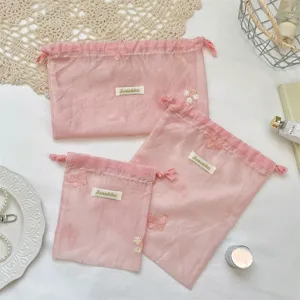 Roze organza opbergzak met trekkoord, voorzien van delicate vlinderborduurwerk en bloemen.