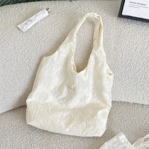 Detail shot of a cream floral embroidered canvas vest bag on a soft cozy textured fleece background.