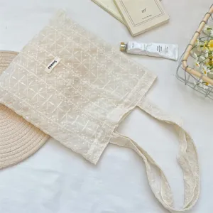Detail view of the beige embroidered lace tote bag, showcasing delicate floral fabric and label.