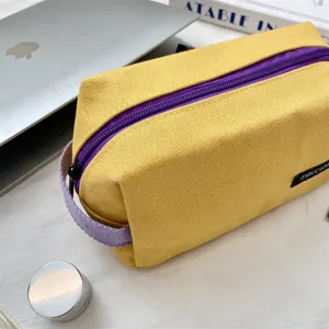 Dettaglio astuccio in tela, borsa portaoggetti gialla minimalista con zip viola e manico.