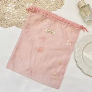 Roze organza trekkoord opbergtas met delicate vlinder- en madeliefjesborduurdetails.