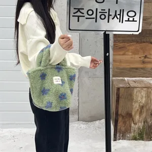 Green fluffy plush handbag winter cute small tote bag with blue floral pattern detail in outdoor scene.