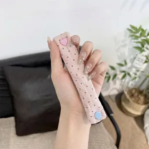 Cute pink polka dot cable organizer strap with heart snap button for neat earphone cord storage.