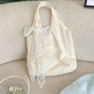 Gros plan du sac cabas en toile crème avec un nœud en dentelle délicat et un tissu texturé.