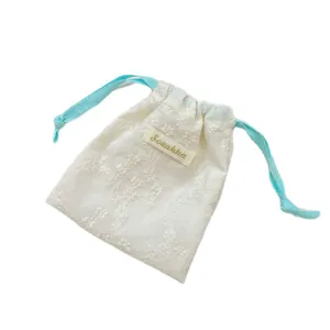 Pochette brodée de fleurs blanches avec cordons bleu clair pour ranger vos bijoux.