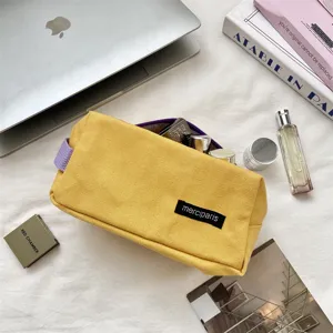 Primo piano di un astuccio minimalista in tela gialla con cerniera viola e etichetta logo.