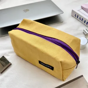 Dettaglio dell'astuccio in tela gialla con cerniera viola per cancelleria e trucco quotidiano.