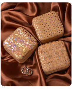 Detailed view of portable square cork jewelry box with foil patterns and satin background.