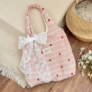 Pink striped tote bag detail with red heart embroidery and white lace bow decoration.