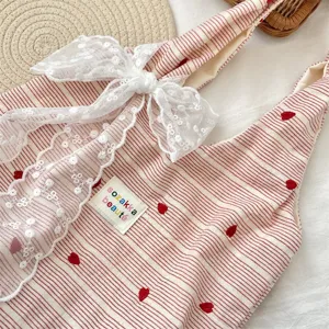 Close-up detail of cute red striped tote bag with red heart embroidery and white lace bow.