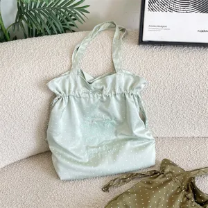 Detalle de bolso de satén verde con lunares, bordado floral delicado y textura suave.