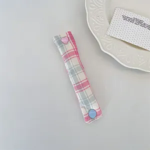 Plaid fabric cable organizer strap with cute heart snap button for tidy desktop storage.