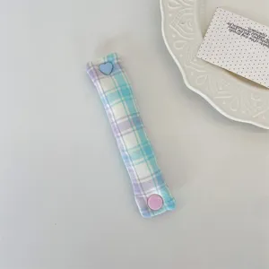 Plaid earphone cable organizer strap with cute heart snap button for tidy desktop storage.