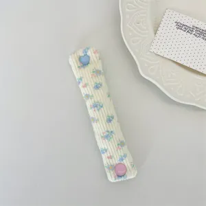 Floral corduroy earphone cable organizer strap with cute heart and round button design.