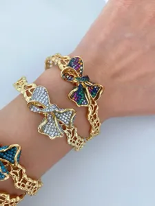 Nahaufnahme von funkelnden bunten Pavé-Kristall-Schleifen-Armreifen am Handgelenk, gold.