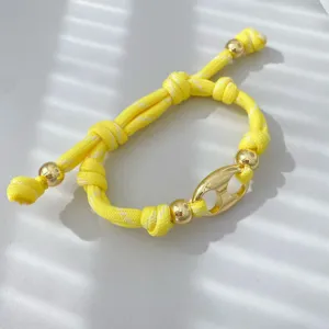 Nahaufnahme des gelben geflochtenen Armbands mit polierten goldenen Perlen und einem Design-Detail.