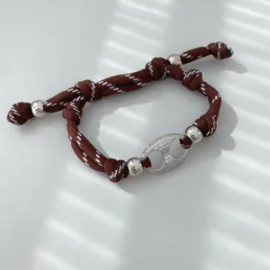 Detailansicht eines braunen geflochtenen Armbands mit Silberperlen und Pavé-Diamant-Mittelstück.