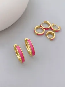 Nahaufnahme von vergoldeten kleinen Creolen mit rosa Emaille, minimalistisches Schmuck Detail.