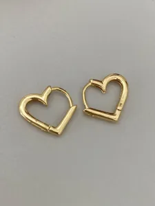 Close-up detail of minimalist gold heart hoop earrings showing polished metal surface.