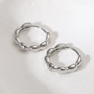 Close-up of silver wavy geometric hoop earrings with a polished minimalist finish