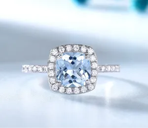 Nahaufnahme eines funkelnden hellblauen Kissen-Edelsteinrings mit strahlendem Diamantkranz.