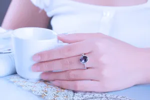 Primo piano di anello in argento con gemma ovale scura e montatura luminosa scintillante.