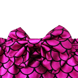 Close-up detail of children's pink mermaid scale swimsuit fabric with matching bow.