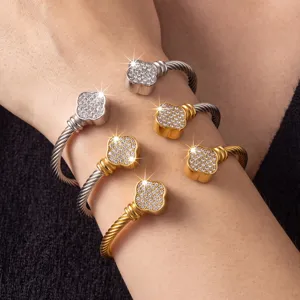 Close-up detail of luxury rhinestone four-leaf clover cable cuff bracelets on wrist.