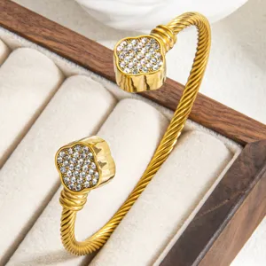 Gold-plated twisted cable cuff bracelet with paved crystal clover ends, minimalist luxury style.