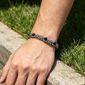 Closeup detail of men stainless steel black bead woven chain bracelet worn on wrist outdoor scene.