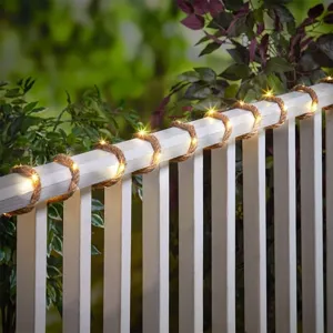 Guirnalda de luces solares de cuerda de cáñamo en valla de madera blanca para decoración exterior.