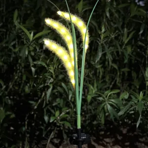Detailed view of solar LED foxtail grass garden light glowing warm yellow at night outdoors.