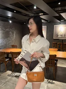 Detailed lifestyle view of brown leather underarm bag in modern cafe scene with elegant model.
