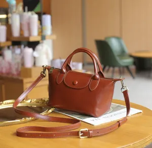 Detail view of the brown leather dumpling handbag with top handles and adjustable strap.