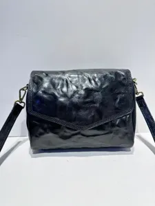 Black genuine leather cross-body bag detail, vintage envelope flap design with metal hardware.