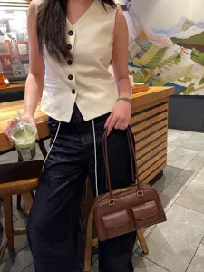 Dettaglio borsa a tracolla in pelle marrone, stile vintage con doppie tasche frontali e cinghie.