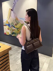 Vista dettagliata di una borsa a spalla in pelle marrone con tasche frontali e dettagli dorati.