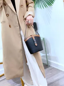 Detail shot of stylish color-blocked leather bucket bag with chain strap and metal turn-lock.