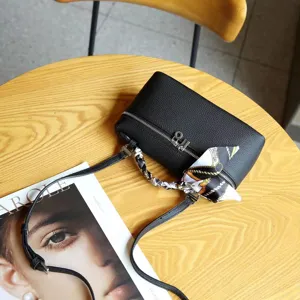 Detail shot of a black leather box bag with a chic silk scarf wrapped handle on a wooden table.