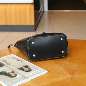 Vista inferior detallada de un bolso cubo de cuero negro con pies metálicos de protección.
