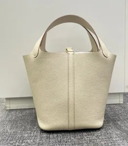 Détail de sac seau en cuir fait main, texture grainée premium, serrure métal, poignées.