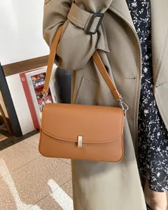 Brown leather underarm bag detail showing premium texture, metal clasp and shoulder strap.