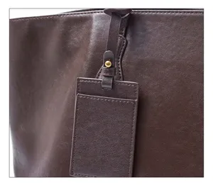 Close-up detail of brown genuine leather tote bag showing fine grain texture and tag.