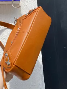 Sac porté épaule de moto en cuir orange avec rivets métalliques, élégante vue détaillée.