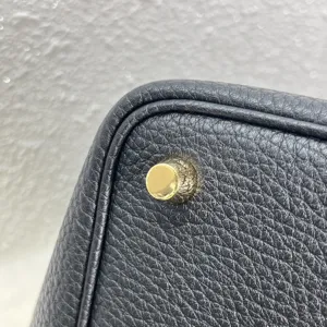 Gros plan du coin d'un sac en cuir noir avec pied en metal dore et bordure propre.