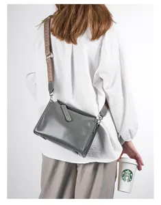 Detail shot of a grey genuine leather crossbody bag with a wide woven strap, stylish look.