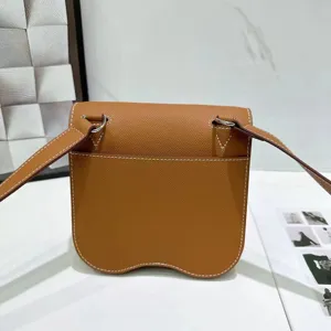 Bruine lederen schouder crossbody tas met uniek gebogen bodemontwerp en zilveren hardware.