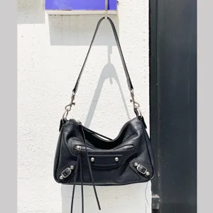 Sac à bandoulière en cuir noir style motard pour femme avec clous métalliques et franges.